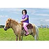happy child ride farm animal brown pony with blue sky in background and beautiful nature