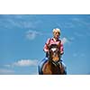 happy woman in sunglasses sitting on horse farm animal outdoors with blue sky in background