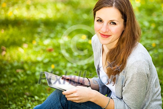 Young woman using her tablet computer while relaxing outdoors in a park on a lovely spring day Young woman using her tablet computer while relaxing outdoors in a park on a lovely spring day