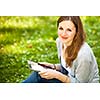 Young woman using her tablet computer while relaxing outdoors in a park on a lovely spring day