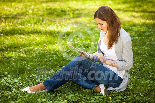 Young woman using her tablet computer while relaxing outdoors in a park on a lovely spring day