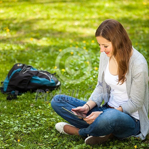 Young woman using her tablet computer while relaxing outdoors in a park on a lovely spring day Young woman using her tablet computer while relaxing outdoors in a park on a lovely spring day