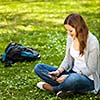 Young woman using her tablet computer while relaxing outdoors in a park on a lovely spring day