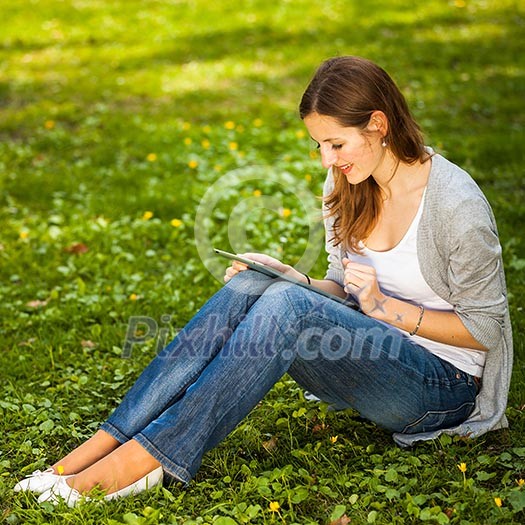 Young woman using her tablet computer while relaxing outdoors in a park on a lovely spring day Young woman using her tablet computer while relaxing outdoors in a park on a lovely spring day