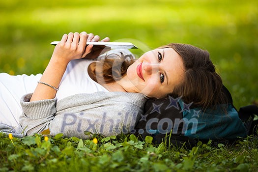 Young woman using her tablet computer while relaxing outdoors in a park on a lovely spring day Young woman using her tablet computer while relaxing outdoors in a park on a lovely spring day