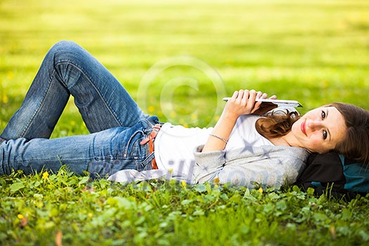 Young woman using her tablet computer while relaxing outdoors in a park on a lovely spring day Young woman using her tablet computer while relaxing outdoors in a park on a lovely spring day