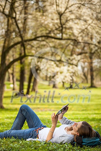 Young woman using her tablet computer while relaxing outdoors in a park on a lovely spring day Young woman using her tablet computer while relaxing outdoors in a park on a lovely spring day