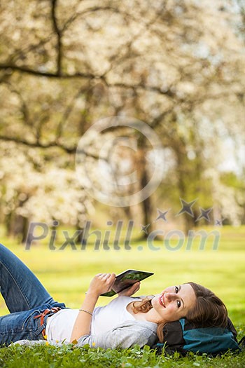 Young woman using her tablet computer while relaxing outdoors in a park on a lovely spring day Young woman using her tablet computer while relaxing outdoors in a park on a lovely spring day