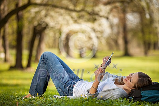 Young woman using her tablet computer while relaxing outdoors in a park on a lovely spring day Young woman using her tablet computer while relaxing outdoors in a park on a lovely spring day