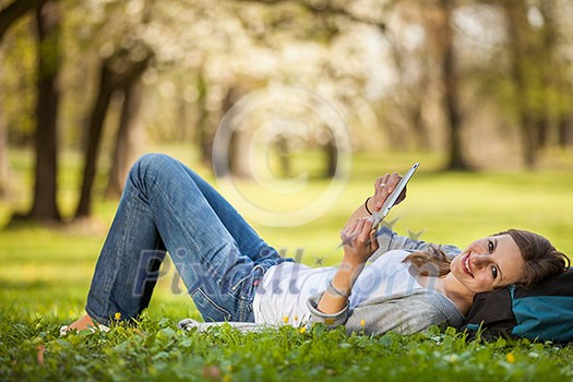 Young woman using her tablet computer while relaxing outdoors in a park on a lovely spring day Young woman using her tablet computer while relaxing outdoors in a park on a lovely spring day