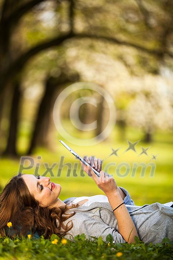 Young woman using her tablet computer while relaxing outdoors in a park on a lovely spring day Young woman using her tablet computer while relaxing outdoors in a park on a lovely spring day