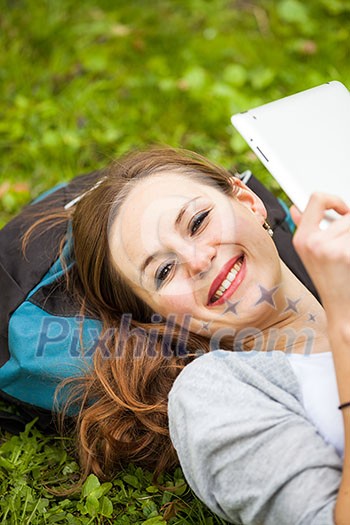 Young woman using her tablet computer while relaxing outdoors in a park on a lovely spring day Young woman using her tablet computer while relaxing outdoors in a park on a lovely spring day