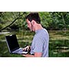 one young businessman working on laptop outdoor with green nature in background