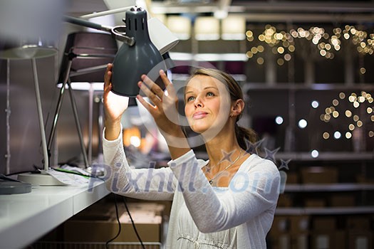 Pretty, young woman choosing the right lamp for her apartment in a modern home furnishings store (color toned image; shallow DOF) Pretty, young woman choosing the right lamp for her apartment in a modern home furnishings store (color toned image; shallow DOF)