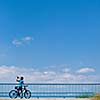 Background for poster or advertisment pertaining to cycling/sport/outdoor activities - female cyclist during a halt on a bridge against blue sky (color toned image)