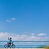 Background for poster or advertisment pertaining to cycling/sport/outdoor activities - female cyclist during a halt on a bridge against blue sky (color toned image)