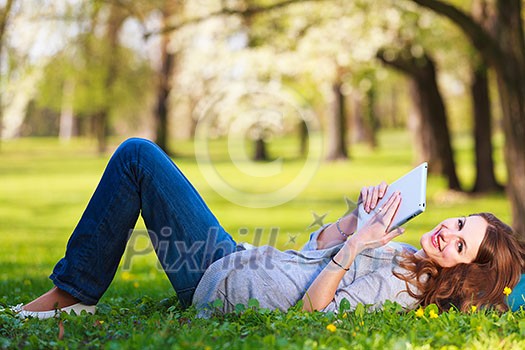 Young woman using her tablet computer while relaxing outdoors in a park on a lovely spring day Young woman using her tablet computer while relaxing outdoors in a park on a lovely spring day