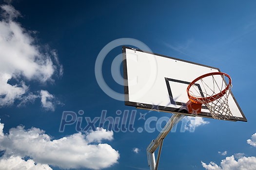Basketball hoop against lovely blue summer sky with some fluffy white clouds Basketball hoop against lovely blue summer sky with some fluffy white clouds
