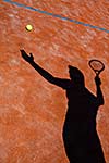 shadow of a tennis player in action on a tennis court (conceptual image with a tennis ball lying on the court and the shadow of the player positioned in a way he seems to be playing it)
