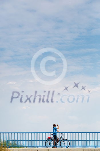 Background for poster or advertisment pertaining to cycling/sport/outdoor activities - female cyclist during a halt on a bridge against blue sky (color toned image) Background for poster or advertisment pertaining to cycling/sport/outdoor activities - female cyclist during a halt on a bridge against blue sky (color toned image)