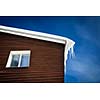 Winter/mountain concept: closeup of a wooden cottage roof covered with snow and icicles against blue sky