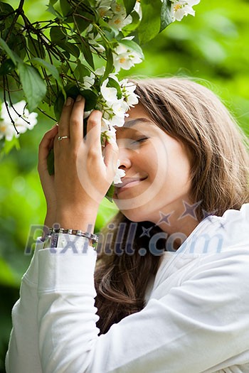 Beautiful young woman smelling white jasmin flowers Beautiful young woman smelling white jasmin flowers