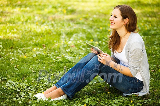 Young woman using her tablet computer while relaxing outdoors in a park on a lovely spring day Young woman using her tablet computer while relaxing outdoors in a park on a lovely spring day
