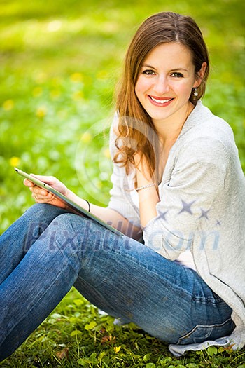 Young woman using her tablet computer while relaxing outdoors in a park on a lovely spring day Young woman using her tablet computer while relaxing outdoors in a park on a lovely spring day