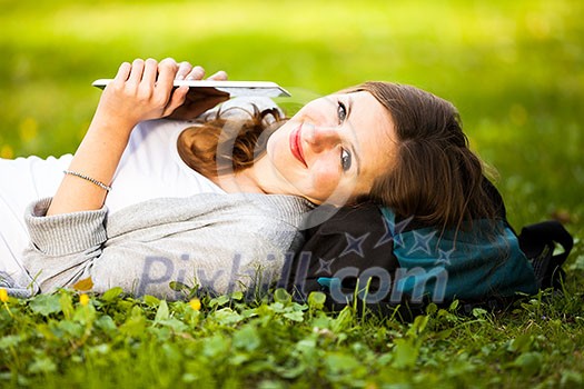 Young woman using her tablet computer while relaxing outdoors in a park on a lovely spring day Young woman using her tablet computer while relaxing outdoors in a park on a lovely spring day
