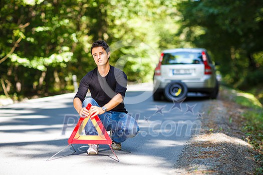 Handsome young man with his car broken down by the roadside, setting the safety triangle Handsome young man with his car broken down by the roadside, setting the safety triangle