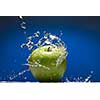 Green apple with water splash on blue background