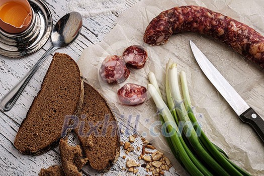 Rustic breakfast. Sausage, green onion and bread on a wooden table. Rustic breakfast. Sausage, green onion and bread on a wooden table.