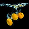 Fresh tangerines dropped into water with bubbles on black