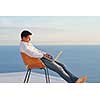 handsome young man relaxing and working on laptop computer at home balcony while looking sunset