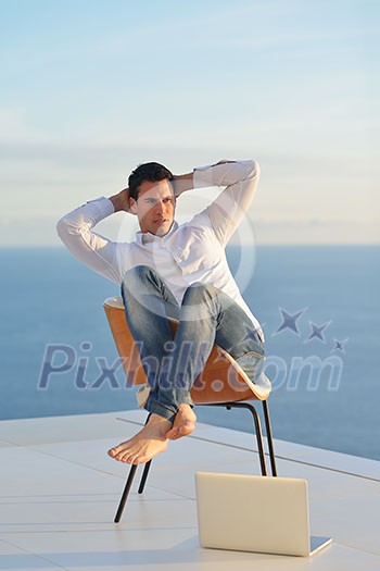 handsome young man relaxing and working on laptop computer at home balcony while looking sunset handsome young man relaxing and working on laptop computer at home balcony while looking sunset