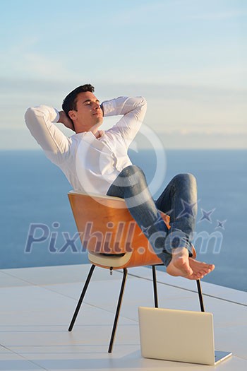 handsome young man relaxing and working on laptop computer at home balcony while looking sunset handsome young man relaxing and working on laptop computer at home balcony while looking sunset