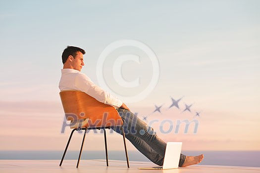 handsome young man relaxing and working on laptop computer at home balcony while looking sunset handsome young man relaxing and working on laptop computer at home balcony while looking sunset