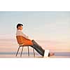 handsome young man relaxing and working on laptop computer at home balcony while looking sunset
