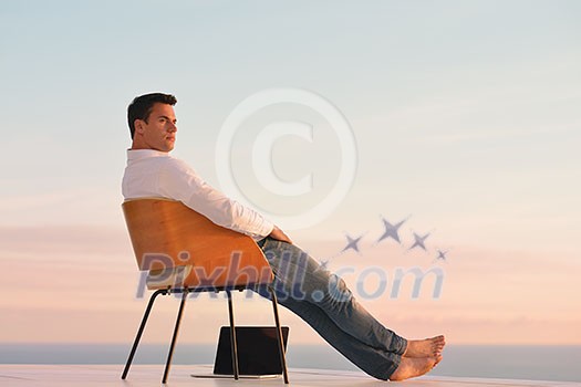 handsome young man relaxing and working on laptop computer at home balcony while looking sunset handsome young man relaxing and working on laptop computer at home balcony while looking sunset
