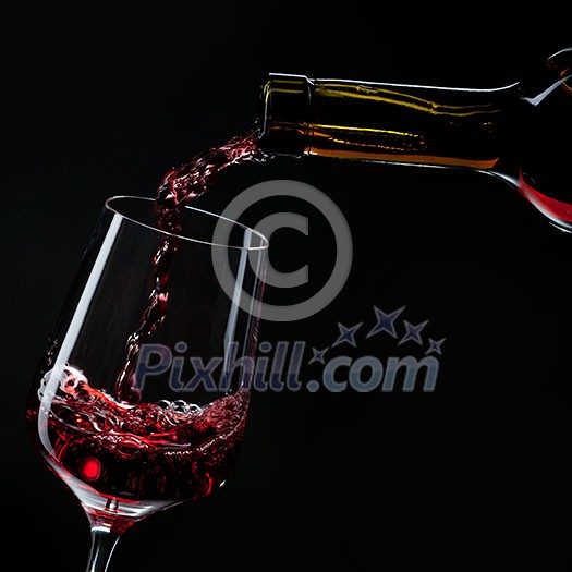 red wine pouring into wine glass isolated on black