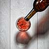 Red wine pouring into glass from bottle on white wooden table. Top view