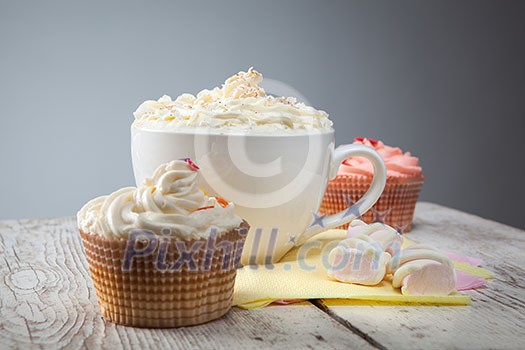 hot chocolate with marshmallows, cream and cupcakes on wooden background hot chocolate with marshmallows, cream and cupcakes on wooden background