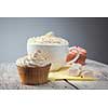 hot chocolate with marshmallows, cream and cupcakes on wooden background