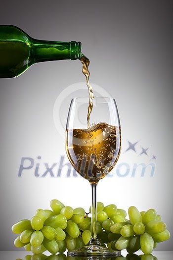White wine pouring into glass from bottle with green grape White wine pouring into glass from bottle with green grape