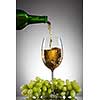 White wine pouring into glass from bottle with green grape