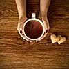 woman holding hot cup of tea with cookies on wooden table