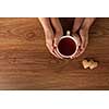 Womans and mens hands holding hot cup of tea on wooden table