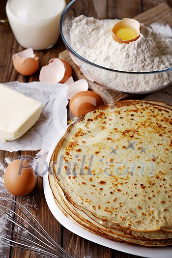 Stack of crepes and ingredients for cooking on a wooden table. Stack of crepes and ingredients for cooking on a wooden table.
