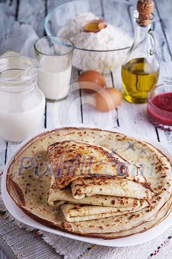 Stack of crepes and ingredients for cooking on a wooden table. Stack of crepes and ingredients for cooking on a wooden table.