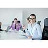 Successful business woman standing with her staff in background at modern bright office